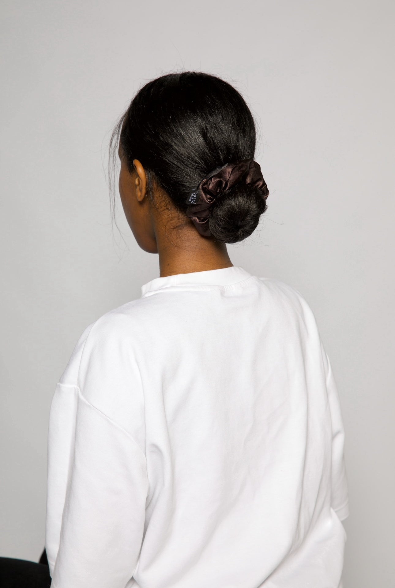 woman turned around, black hair tied in a princess bun with a dark brown satin hair scrunchie