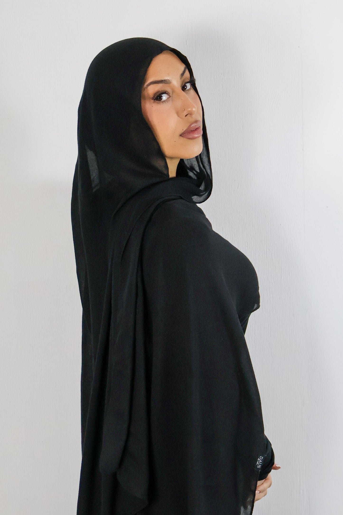 Woman wearing a black hijab and black outfit against a white background