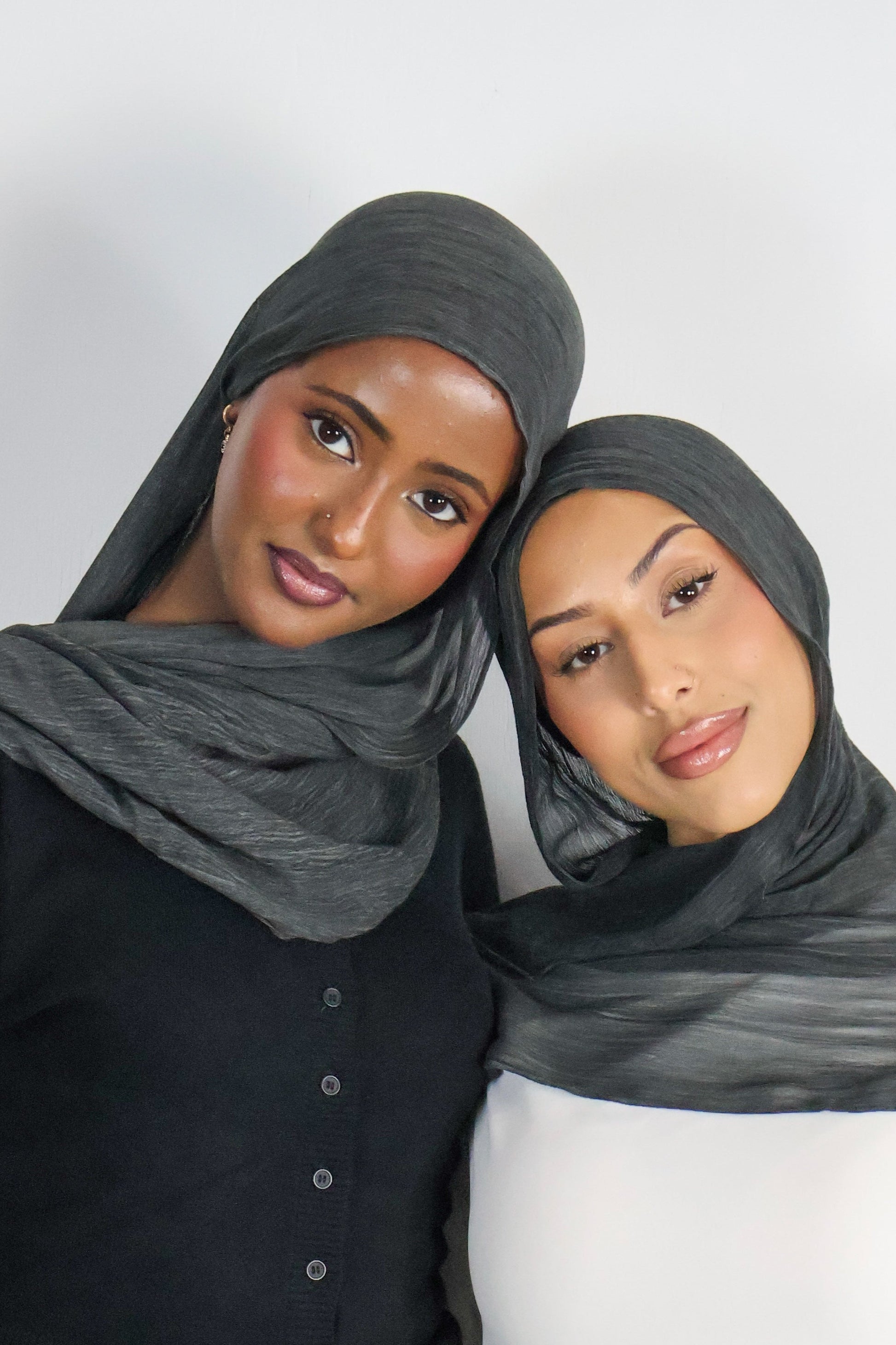 Two women wearing gray hijabs against a white background