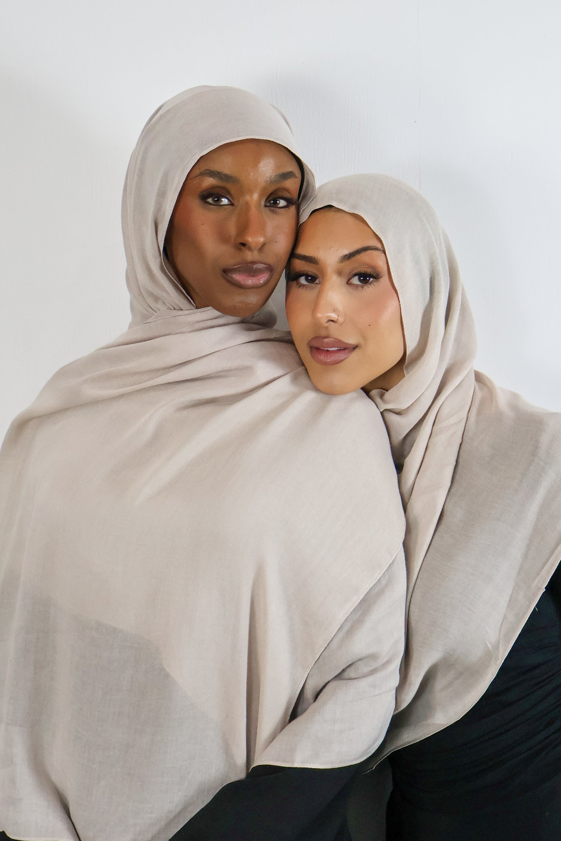 Two women wearing beige hijabs against a white background