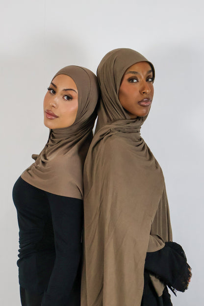 Two women wearing brown hijabs standing back-to-back against a white background