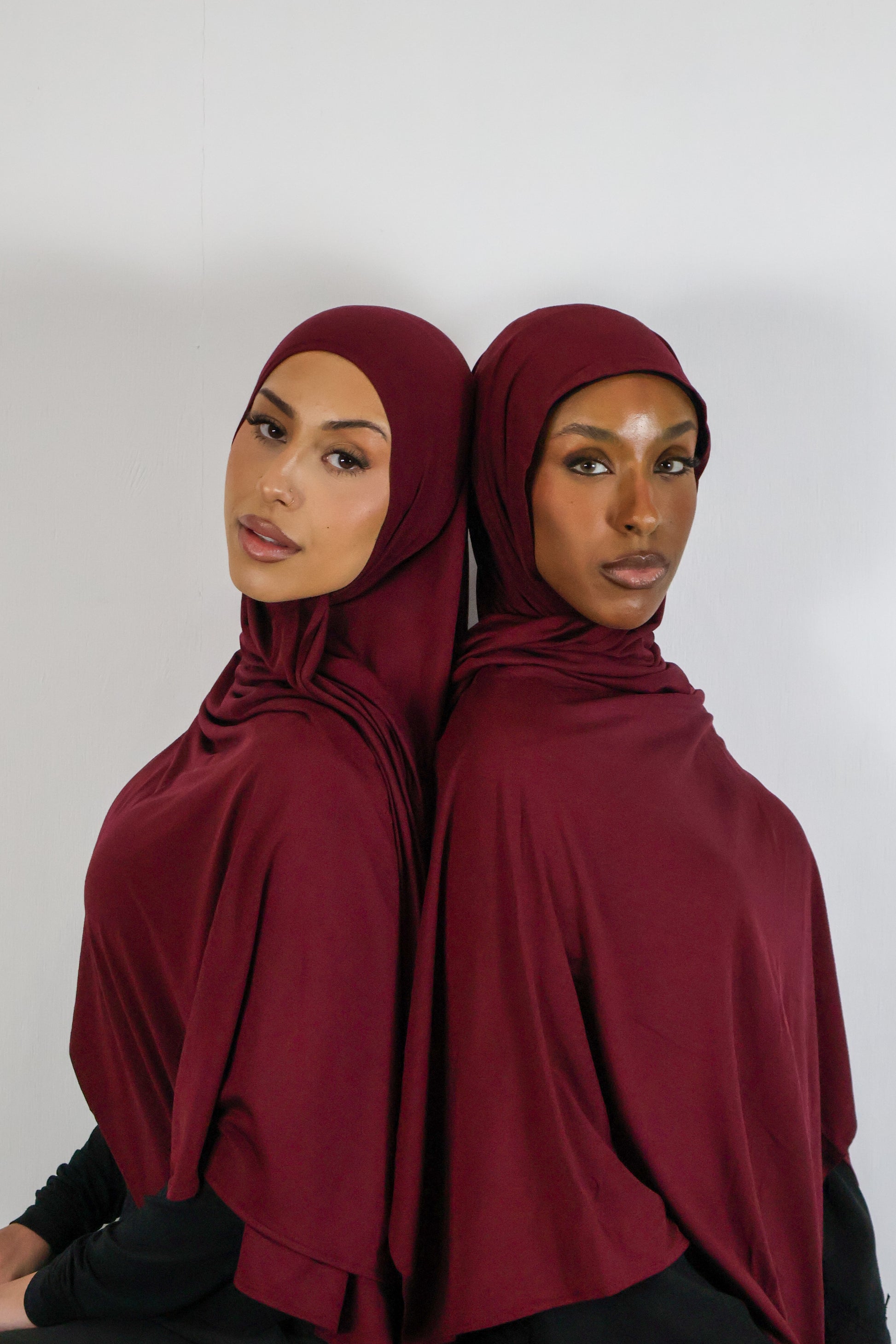 Two women wearing burgundy hijabs against a white background