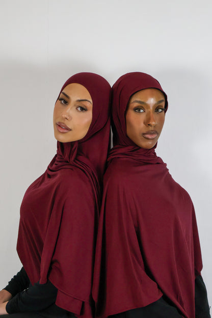 Two women wearing burgundy hijabs against a white background